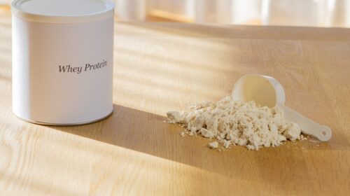 Whey protein powder with scoop on wooden surface