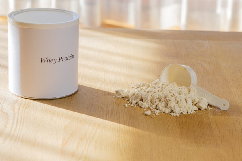 Whey protein powder with scoop on wooden surface