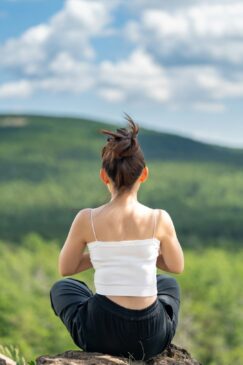 FITPULSE | Mindfulness Meditation Techniques for Wellbeing a woman sitting on top of a rock with her hair in the air