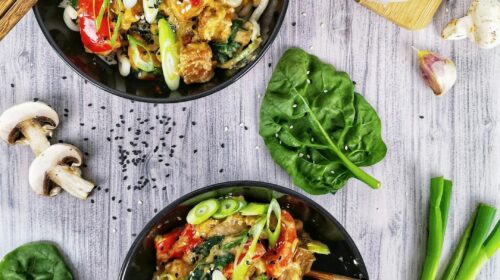 two black bowls filled with food next to chopsticks